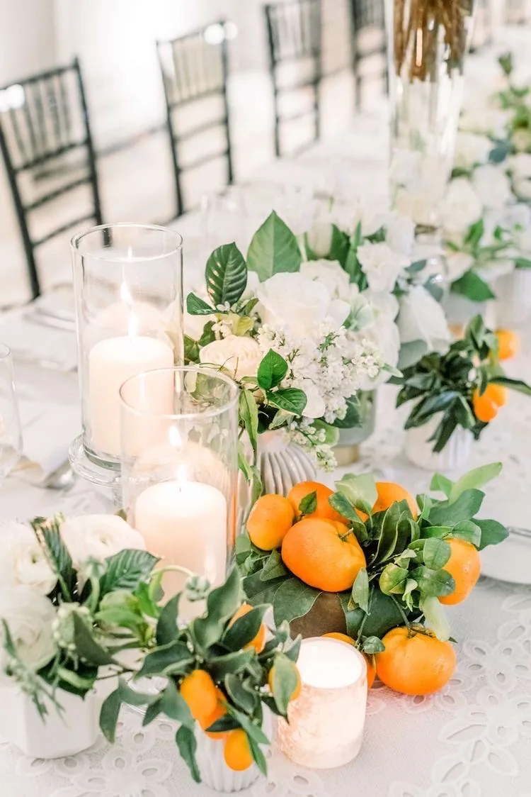 Centro de mesa con velas, flores blancas y naranjas
